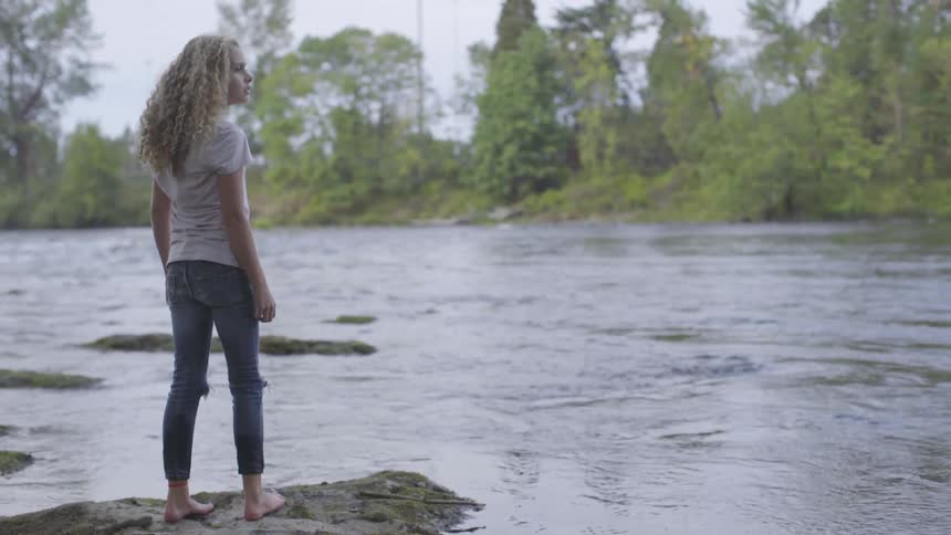 A little girl stands on a rock by a river