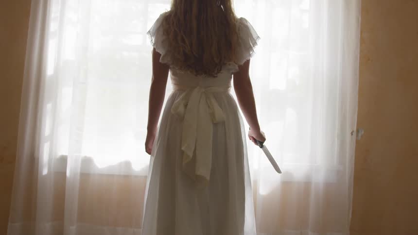 A woman holding a knife at a window