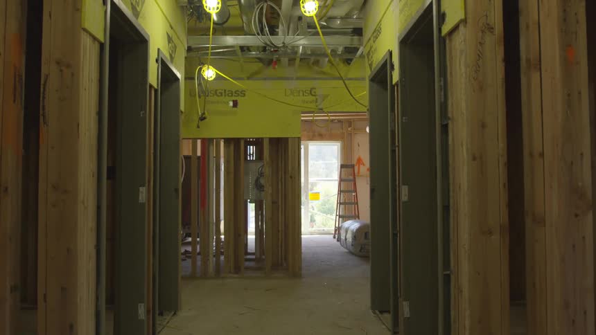 Walking through a unfinished building with exposed walls yellow green lights and a sunny day light pouring through the front of an unfinished home