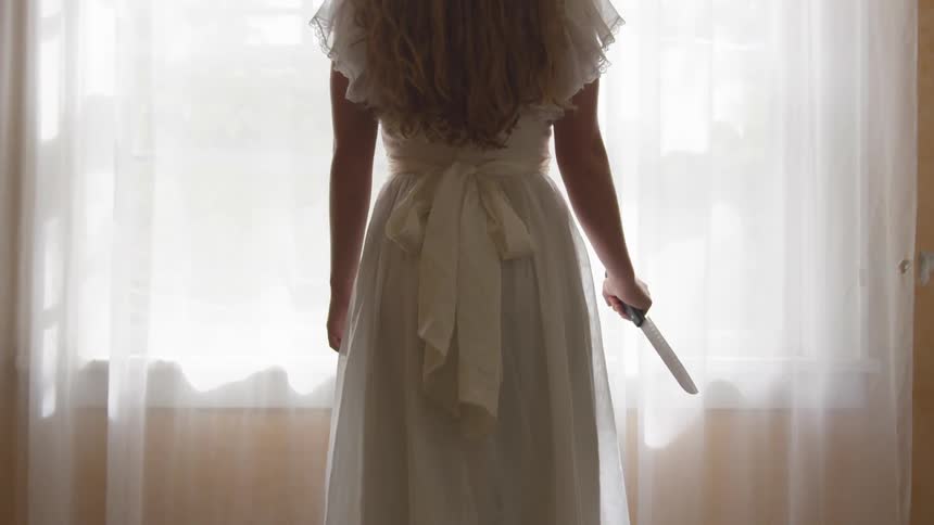 A woman stands by the window with a knife