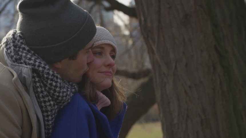 Man kisses a woman next to a tree