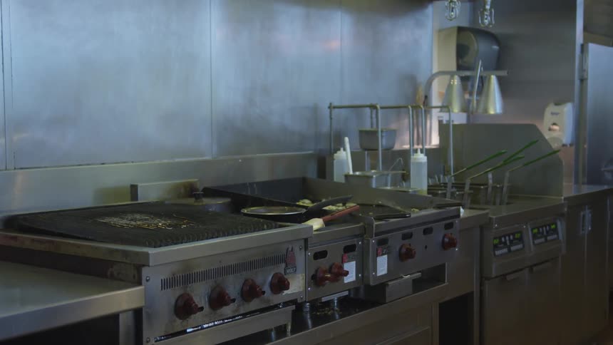 Stoves and fryers line a restaurant kitchen wall