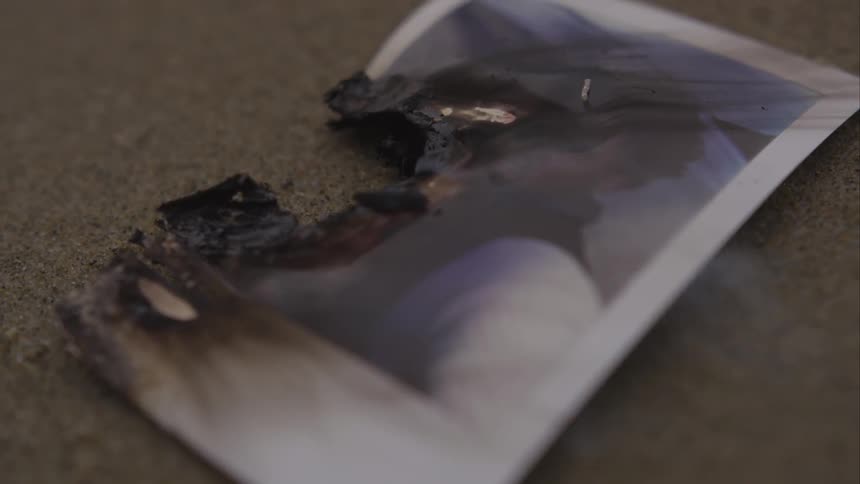 A signed photograph lies smoldering on the ground