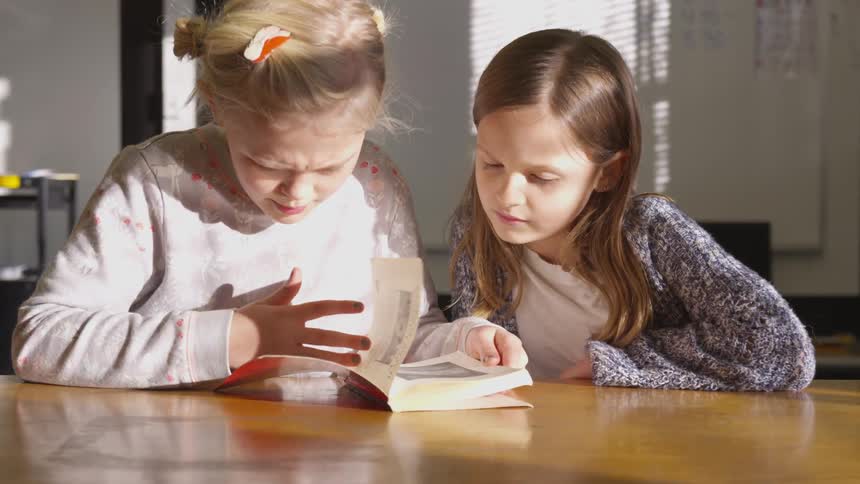 Two girls look at a book on a table