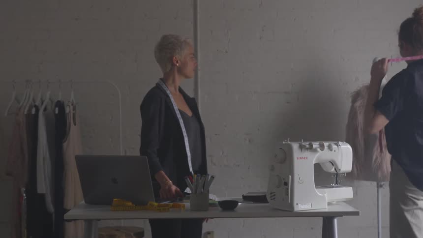 A woman leans over to a laptop and talks to another woman