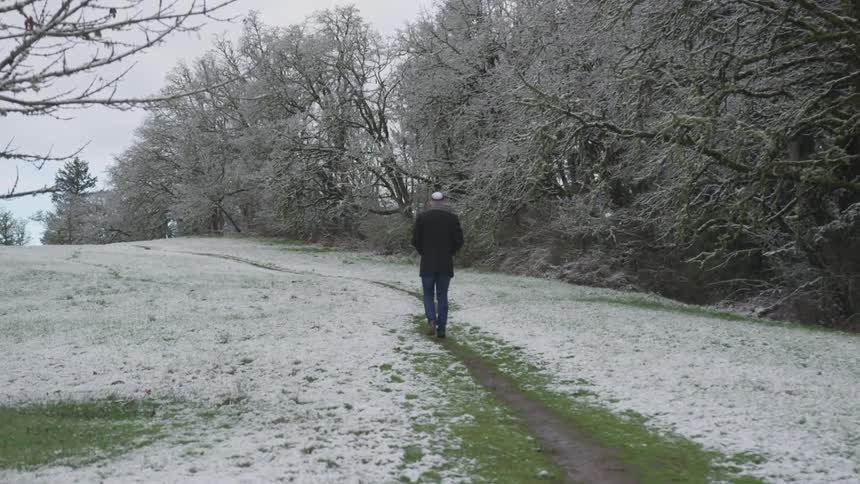 A man is walking on a small trail near the snow covered forest