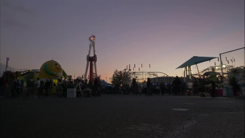 A busy carnival with rides in motion and hundreds of people walking to and fro