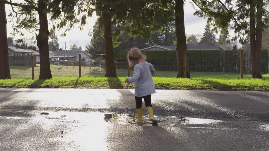 Child wearing rain boots splashes in a puddle while the sun shines