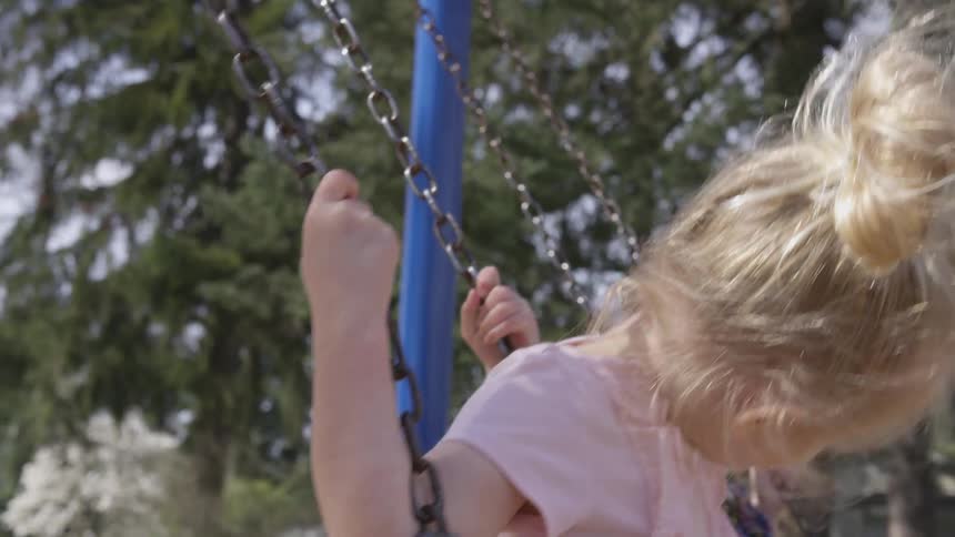 Two little girls swing on a blue swing set