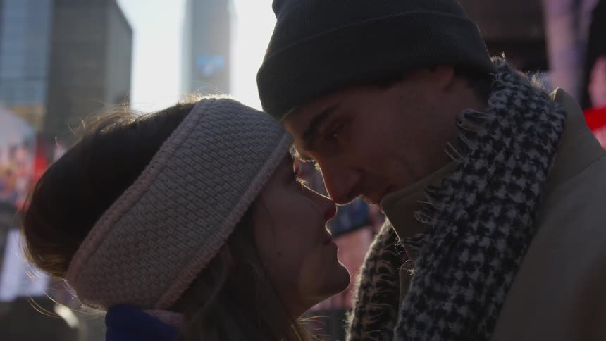A couple stands nose to nose and smile at each other on a city sidewalk