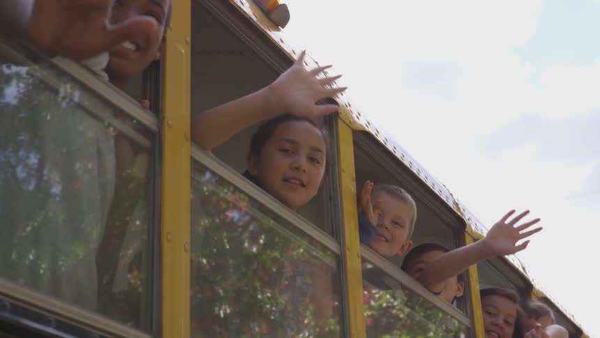 Children lean out bus window and wave