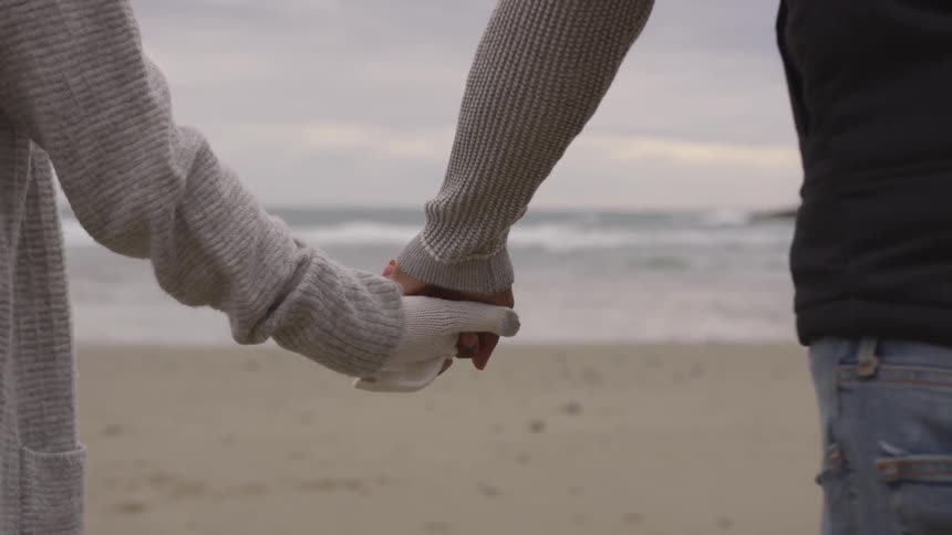 A man and woman are holding hands on the beach
