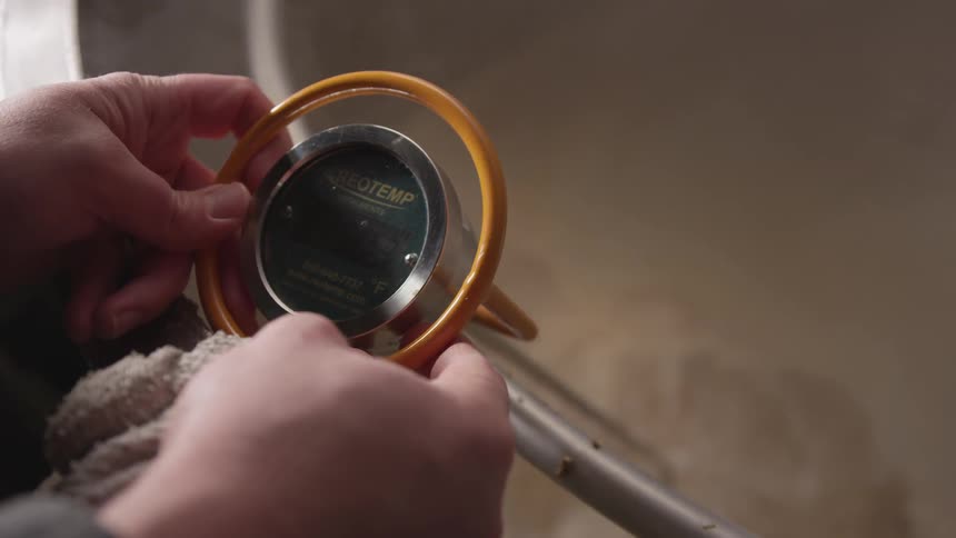 A thermometer is in two hands as it measures the temperature of a large pot below