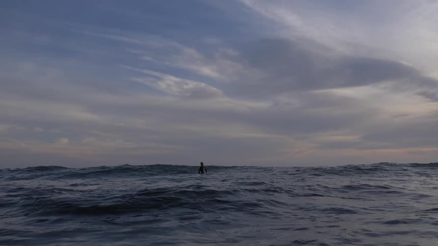 Closeup of ocean waves with surfer sitting on a board in the distance