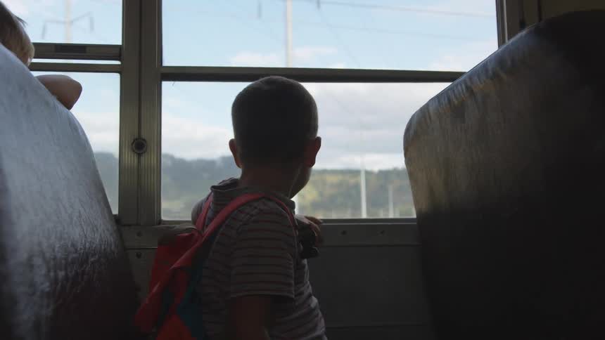 A boy wearing a backpack looks out the school bus window