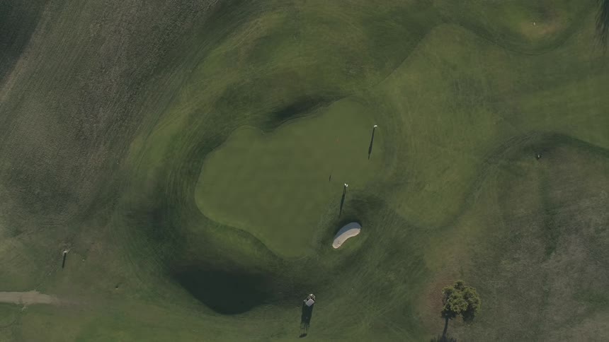 A person walking on a golf green can be seen far below
