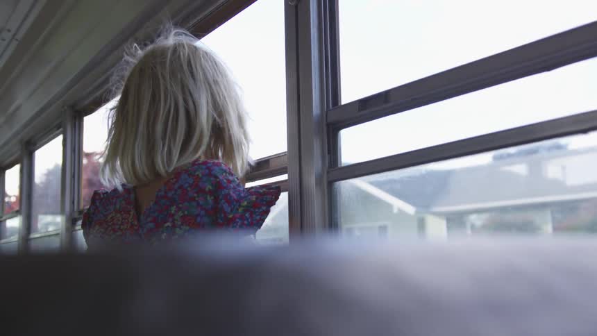 A young girls looks out the window of a school bus