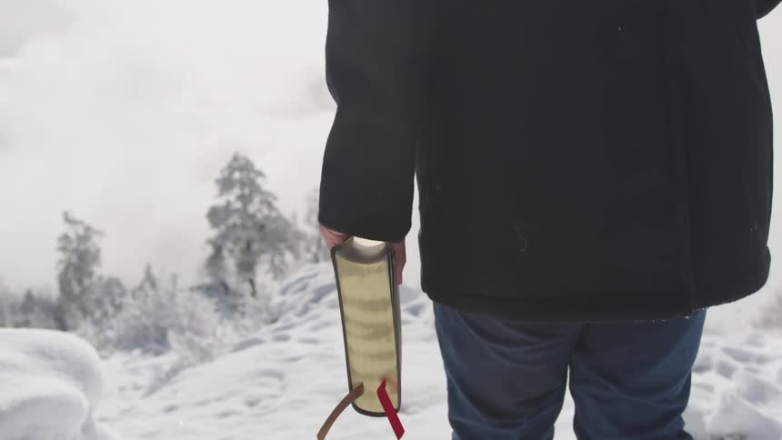 A man walks on snowy ground as he holds a bible in one hand