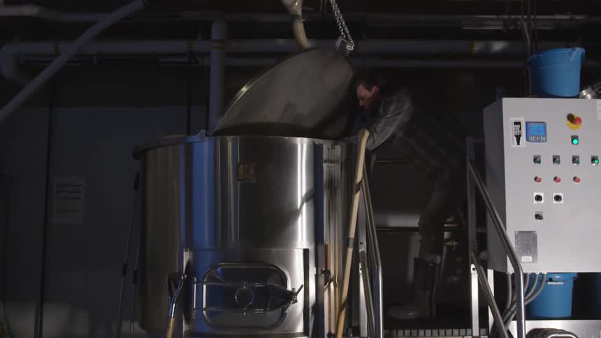 A man leans over a large vat in a brewery