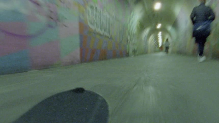 Man skateboarding through a graffiti lined tunnel