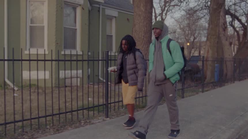 Two people walk together down the neighborhood sidewalk