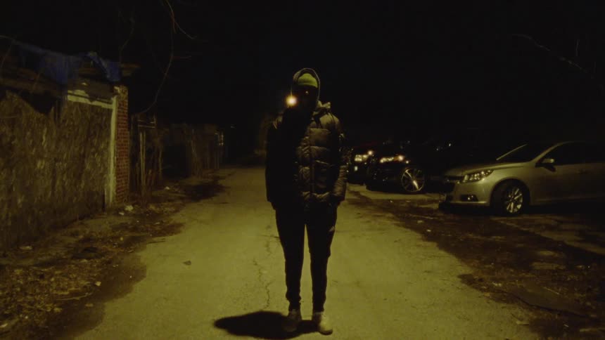 A man in a black coat stands on a sidewalk
