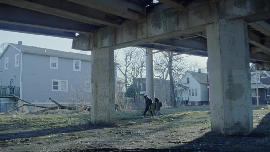 Two people walk under a bridge