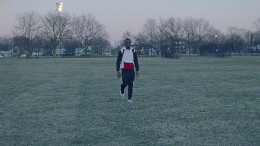 A man walks across a grass field with a backpack at sunset