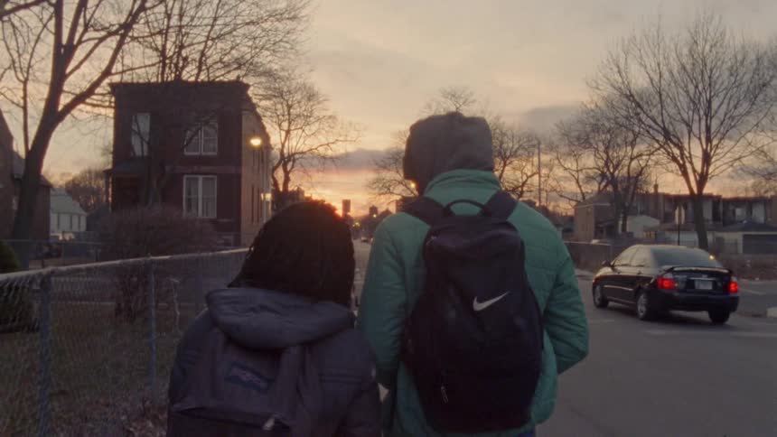 Two people with backpacks walk down the sidewalk