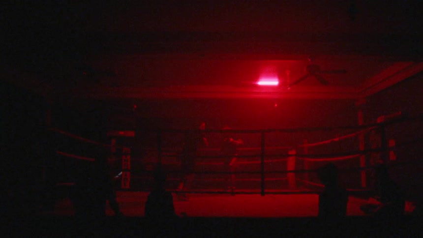 The men are boxing in the ring under red lights