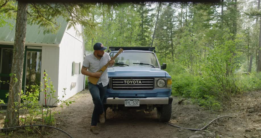 A man is playing an instrument outside by a car