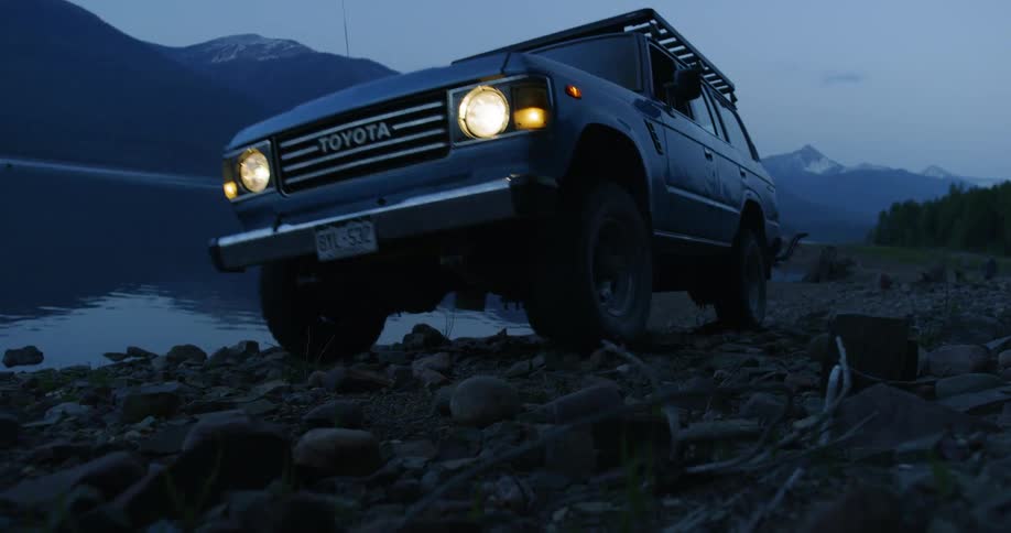 An all terrain vehicle driving on the rocky coast of a lake