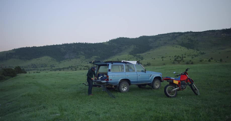 A man stands at the back of a vehicle and takes a drink