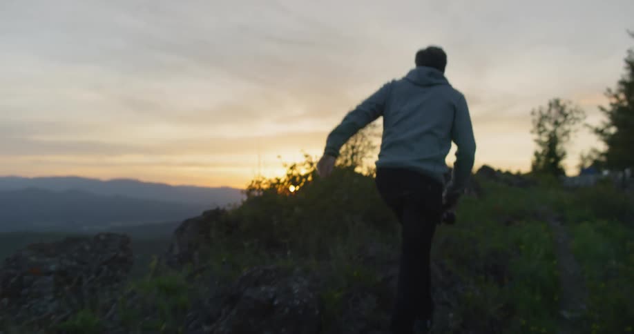 A male points towards the horizon while holding a camera and walking along a hillside