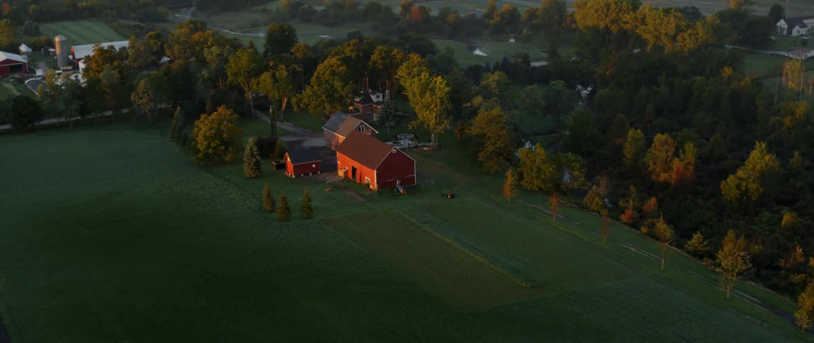 A red barn sits near a house by a large field