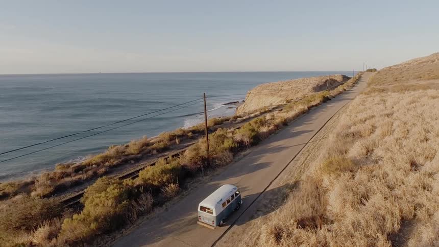 A bus drives down a road by the shore on a sunny day