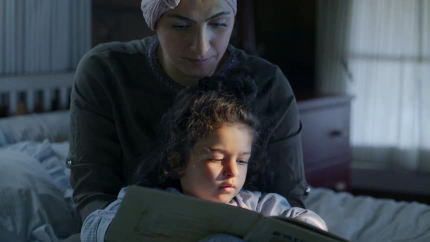 Woman and child reading a book sitting on a bed