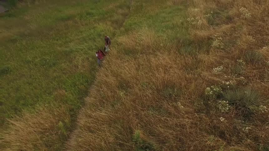 A woman carrying a child while a little girl and man walk behind her on a path through tall grass