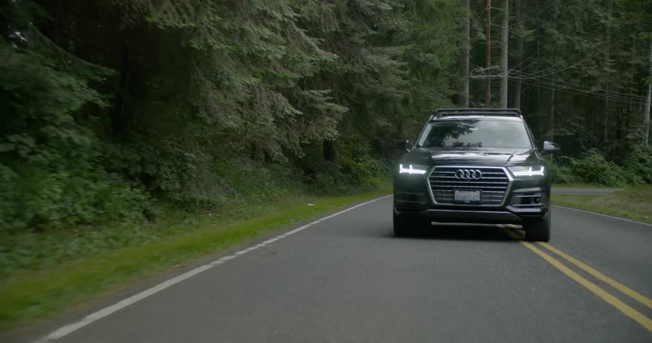 A car is driving on a road by a wooded area
