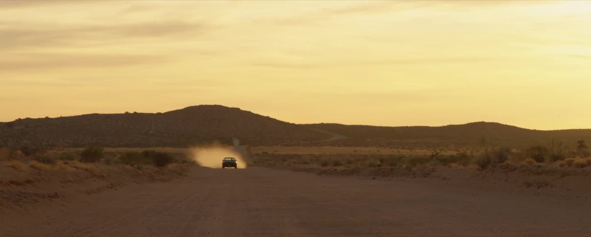 A vehicles drives down the desert trail giving off dust behind