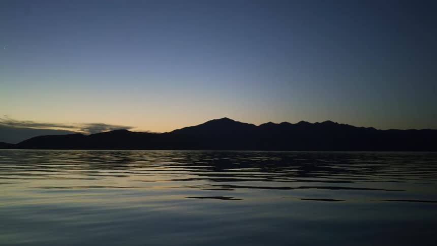 An ocean ripples in the breeze in front of a mountain