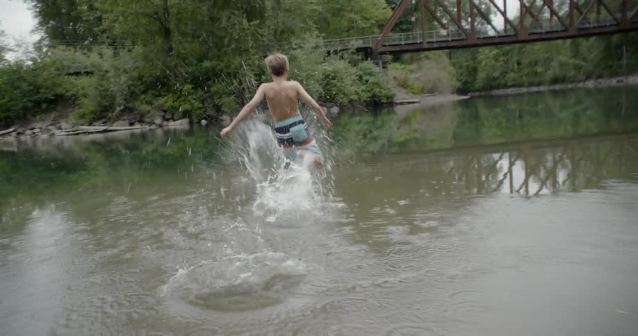 Young boy runs into the creek then jumps into the water