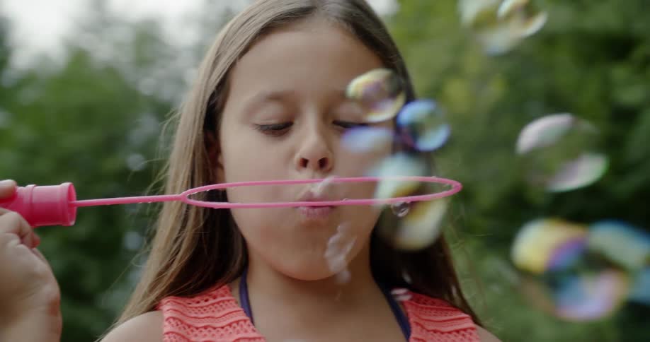 Young girl holds a giant bubble wand as she blows bubbles
