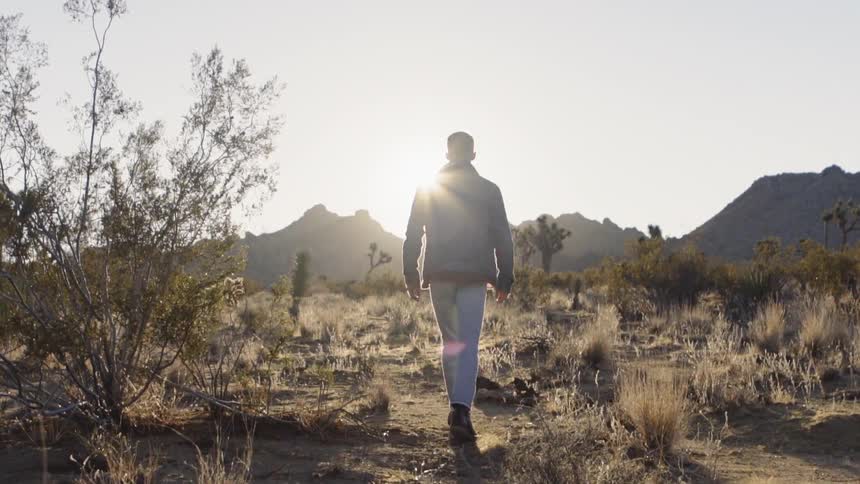 A man is hiking in the desert at sunset