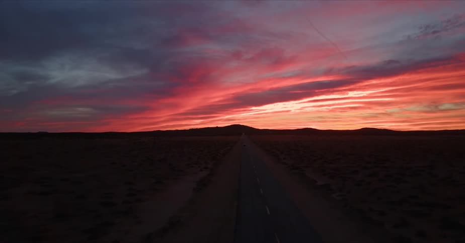 A car drives down a empty road under setting sun