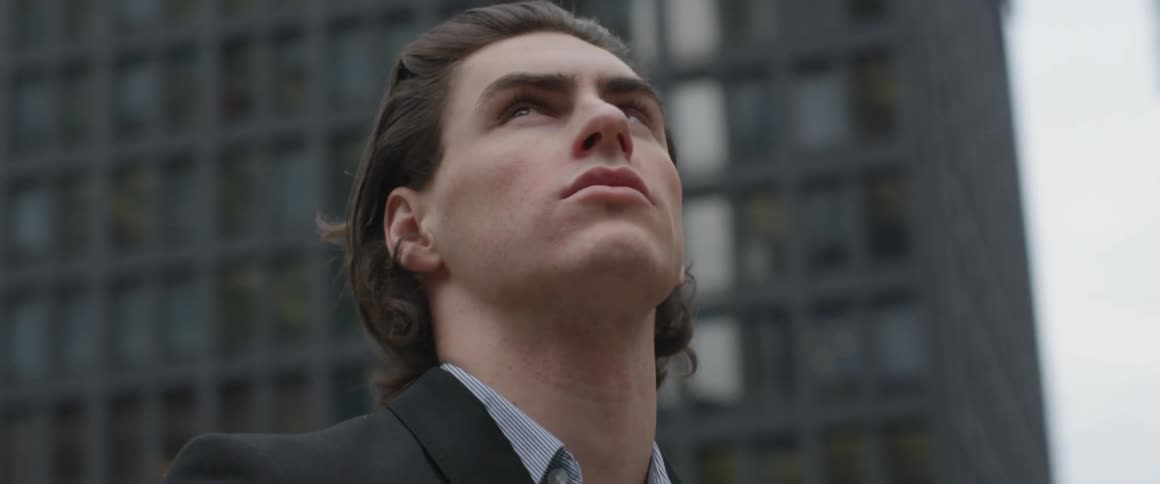 A man in a suit looks up at city skyscrapers