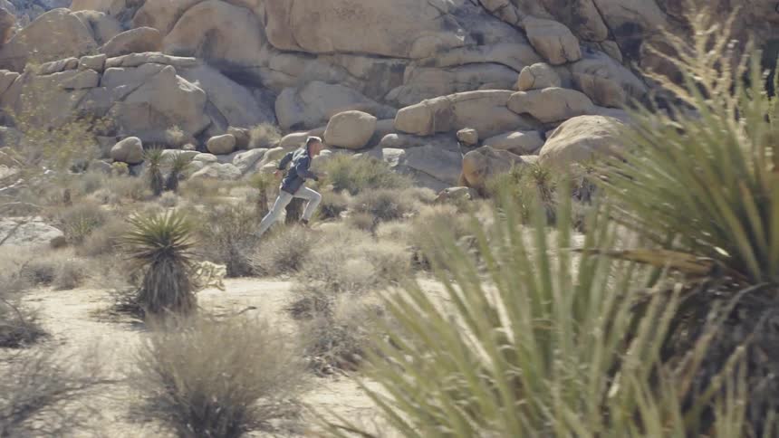 Man runs through wasteland with rocky mountains in background