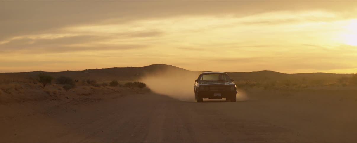 Car driving on a dusty desert road at sunset