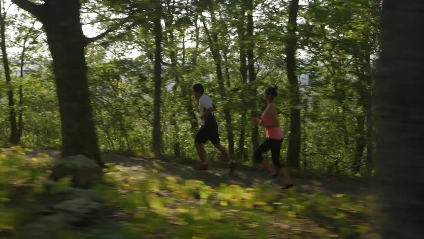 Couple jogging a wooded trail on a sunny day