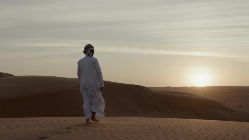 Barefoot person walking through the desert sand dunes during sunrise